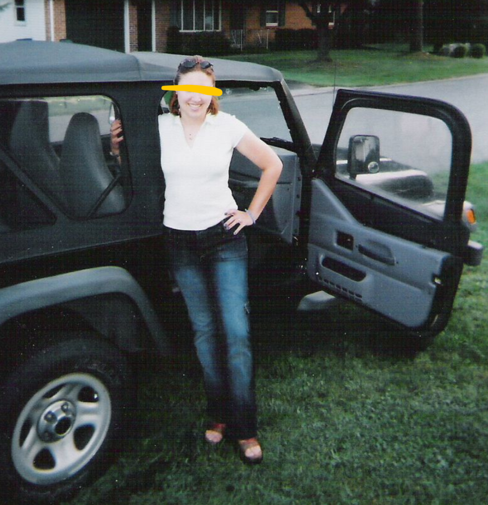Image of a young woman wearing a white short sleeve shirt and jeans, standing by a vehicle and smiling.