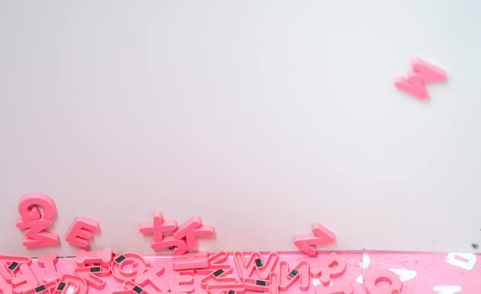 Image of pink letter magnets. Some are magnetized to the white surface while others are on the floor.
