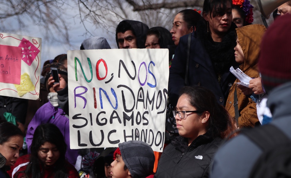 Men and women at a protest holding a sign in Spanish that reads "let's not give up. Let's keep fighting."