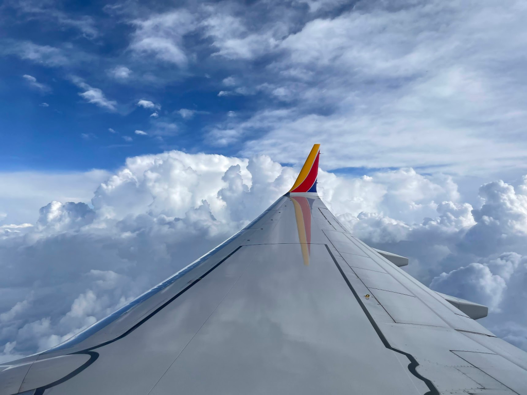View from a plane window, with the airplane's wing extending out toward a cloudy sky.